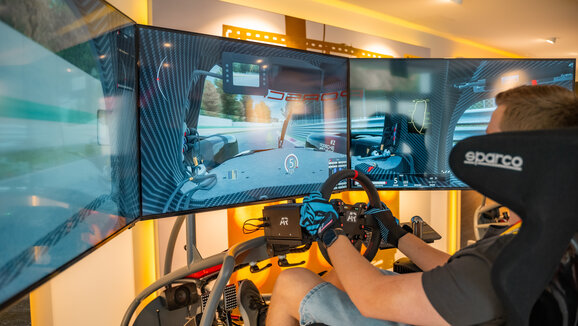 Ein Kunde fährt mit unserem Simulator, man sieht auf verschiedenen Bildschirmen das Cockpit eines Autos, sowie durch die Windschutzscheibe die Rennstrecke
